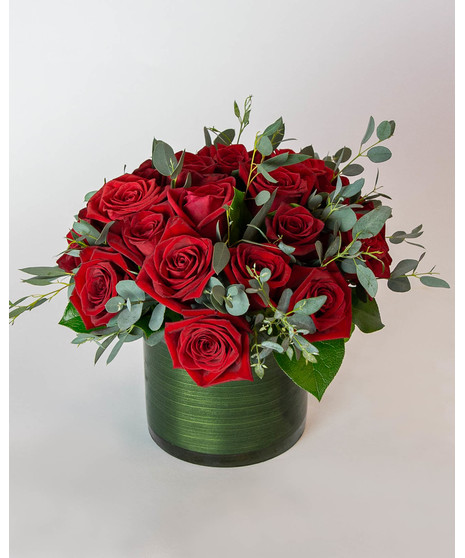 Beautiful roses are arranged in an elegant cylinder glass leaf-lined vase. 