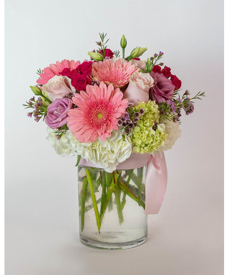 blush and ivory arrangement includes roses, gerbera daisies, lisianthus, hydrangea, and more in a timeless tall cylinder glass vase tied with a silk pink bow. 