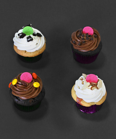 four example cupcakes with pink and green sugar buttons and a variety of chocolate and nutty toppings