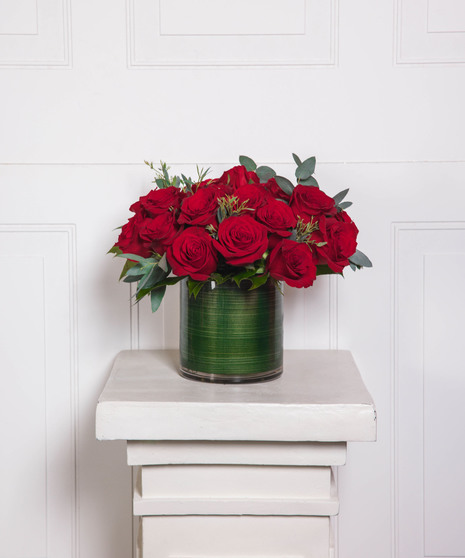 Beautiful roses are arranged in an elegant cylinder glass leaf-lined vase. 