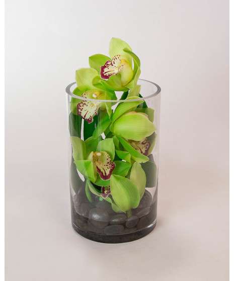 We carefully place an elegant cymbidium orchid stem with a monstera leaf on a bed of river rocks to create this serene arrangement. 