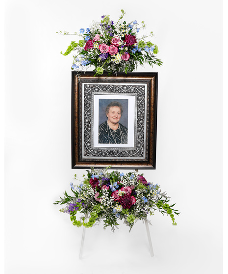Show tribute to a loved one with an array of pink, light blue, and purple flowers surrounding a picture frame at your loved ones funeral service.