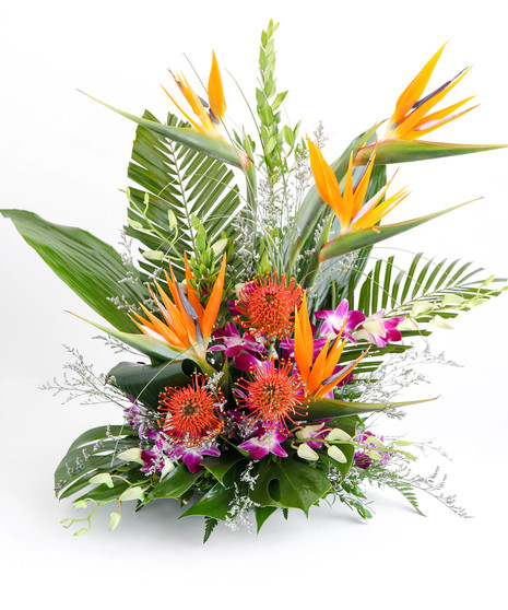 A vibrant floral arrangement featuring orange bird-of-paradise flowers and purple orchids, surrounded by large green leaves, placed on a white surface.