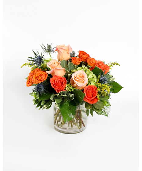 An orange tropical flower arrangement featuring birds of paradise, thistle, and roses. 