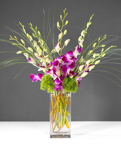 This arrangement includes stunning dendrobium orchids in a vase with exotic greenery.