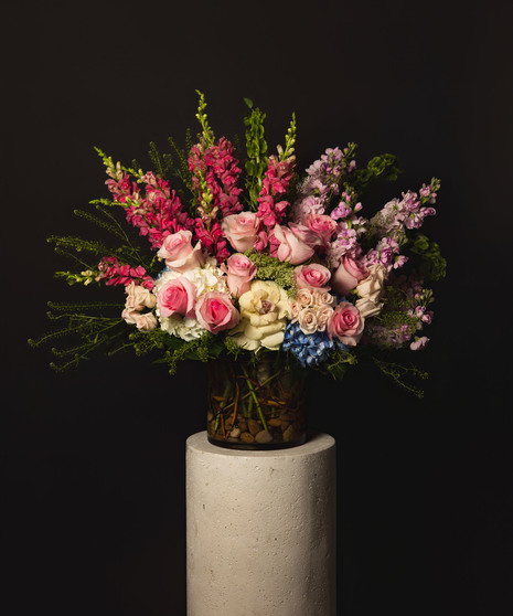This arrangement is artfully designed with white o-hara garden roses, hydrangeas, larkspur, and stock in a low cylinder glass vase accented with river stones. 