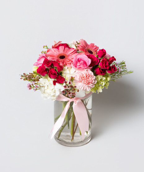 blush and ivory arrangement includes roses, gerbera daisies, lisianthus, hydrangea, and more in a timeless tall cylinder glass vase tied with a silk pink bow. 