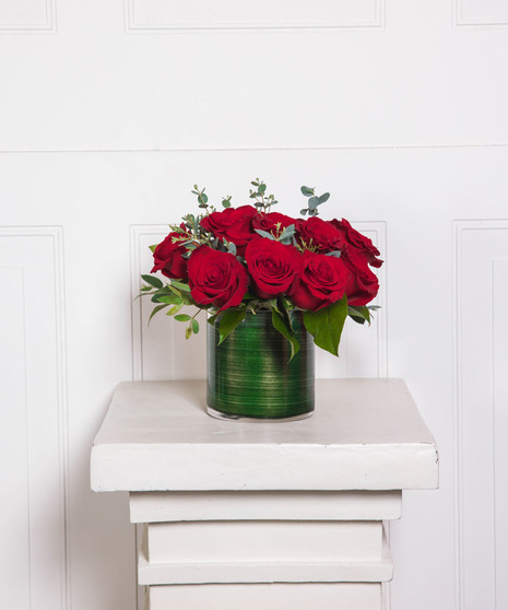 Beautiful roses are arranged in an elegant cylinder glass leaf-lined vase. 