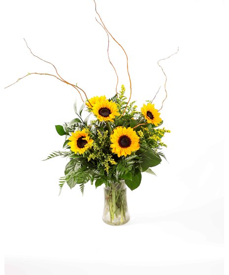 Bright petite sunflowers with cheerful yellow solidago and fresh greenery in a clear, hourglass-shaped glass vase. 