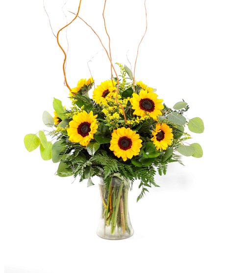 Bright petite sunflowers with cheerful yellow solidago and fresh greenery in a clear, hourglass-shaped glass vase. 