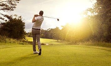 Man swinging golf club on green course with afternoon sunshine